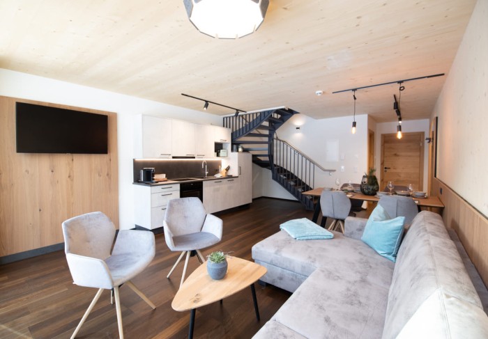 Wohnbereich mit Couch und TV / im Hintergrund die Küchenzeile und der Aufgang in den zweiten Stock